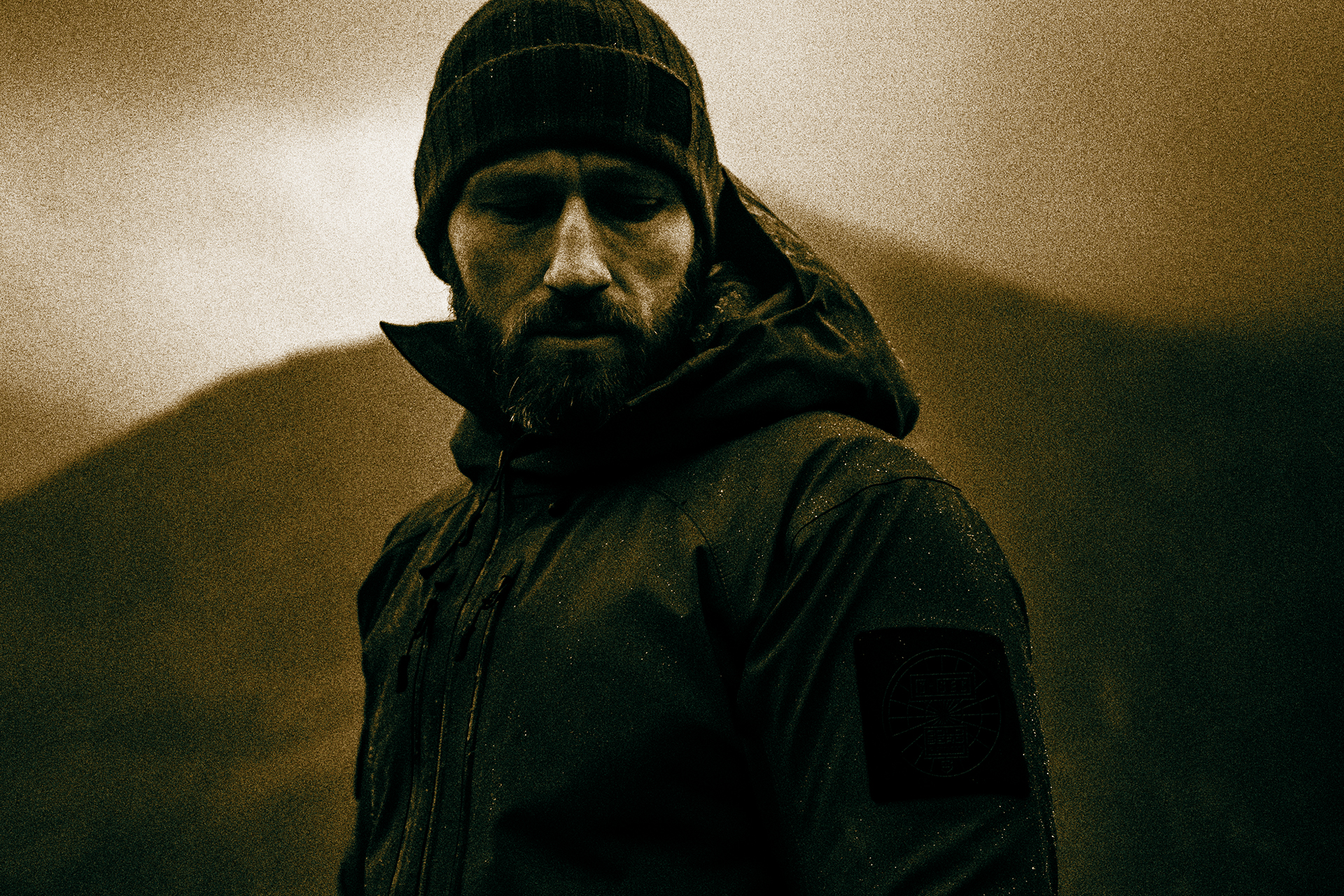 A Goldberg shell jacket worn in low light — sealed hood, storm collar, sleeve patch.